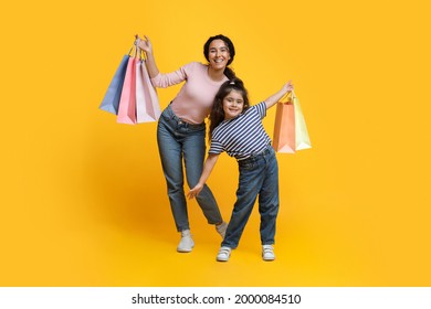 Family Shopping. Cheerful Arab Mom And Little Daughter Posing With Lots Of Bright Shopped Bags, Positive Middle Eastern Mother And Child Standing Over Yellow Studio Background, Copy Space