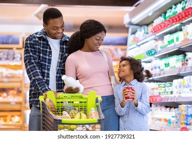 Family shopping concept. Young black parents with pretty daughter selecting food at supermarket. Cheerful black girl with mom and dad buying products at dairy department of big mall