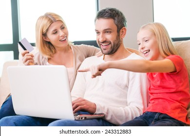 Family Shopping Online. Happy Family Of Three Bonding To Each Other And Smiling While Sitting On The Couch And Shopping Online Together 