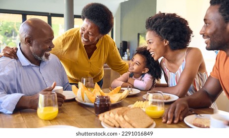 Family Shot With Grandparents Parents And Granddaughter Eating Breakfast Around Table At Home - Powered by Shutterstock