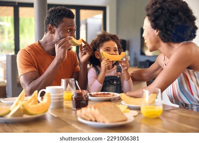 Family Shot With Parents And Daughter At Home Making Funny Faces With Melon Before Eating Breakfast - Powered by Shutterstock