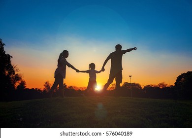 Family Silhouette With Sunset , Family On The Front Of The Sunset In The Sky On A Holiday With Sun Flare On Chatuchak Park At Bangkok City, Thailand. Concept Of Friendly Family.