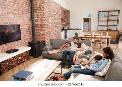 Family Sit On Sofa In Open Plan Lounge Using Technology