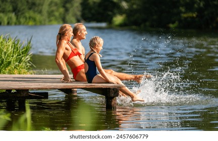 Family sit on a wooden dock by a lake at summer, splashing water with their feet - Powered by Shutterstock