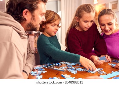 Family Sitting Around Table At Home Doing Jigsaw Puzzle Together