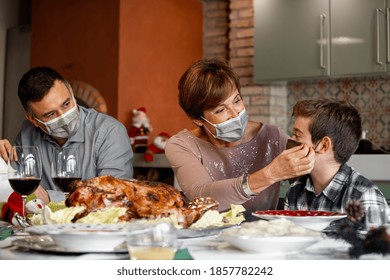 Family sitting at the Christmas Thanksgiving table at home in the year of the Coronavirus Pandemic. Grandmother adjust the surgical mask to her grandson. New rules, Covid outbreak, lockdown. - Powered by Shutterstock