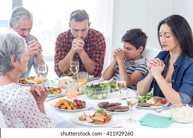 Family sitting at dining table and praying together before meal
