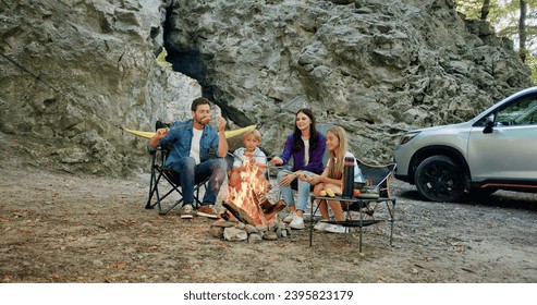 Family sitting near campfire and car on summer evening fry sausages. Children with their parents are resting in woods. Childhood relationship camping. - Powered by Shutterstock