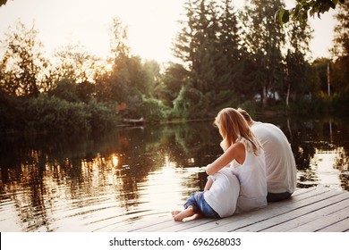 Family Sitting Near Water And Watching The Lake At Sunset