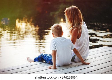 Family Sitting Near Water And Watching The Lake At Sunset