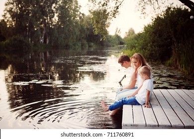 Family Sitting Near Water And Watching The Lake At Sunset