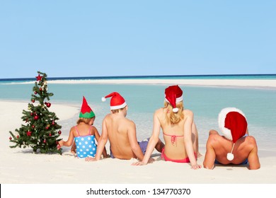 Family Sitting On Beach With Christmas Tree And Hats