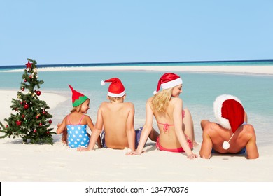 Family Sitting On Beach With Christmas Tree And Hats