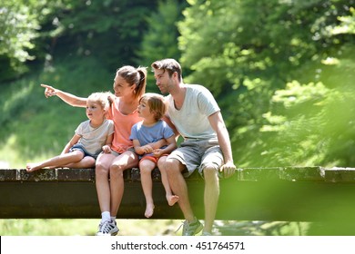 Family Sitting On A Bridge Crossing Mountain River