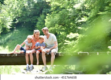 Family Sitting On A Bridge Crossing Mountain River