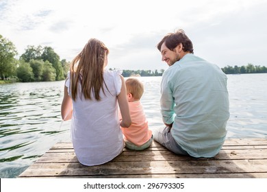 Family Sitting On Jetty Of Pond Or Lake In Summer