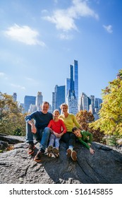 Family Sitting On A Rock In Central Park Manhattan New York On A Sunny Fall Day With Skyscrapers In The Background