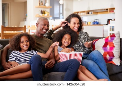 Family Sitting On Sofa At Home Eating Popcorn And Watching Movie Together