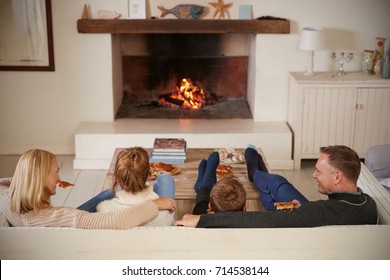 Family Sitting On Sofa In Lounge Next To Open Fire