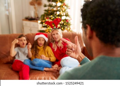 Family Sitting On Sofa Playing Game Of Charades At Christmas Together