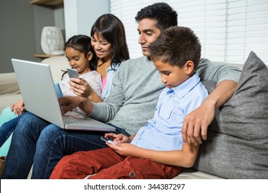 Family Sitting On The Sofa And Using Technology