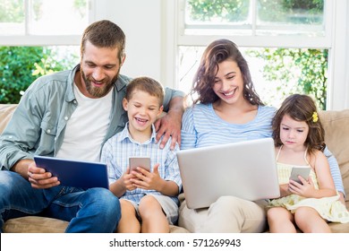 Family Sitting On Sofa And Using A Laptop, Tablet And Phone At Home