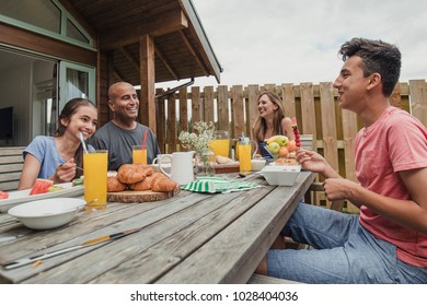 Family Sitting Outside Holdiay Lodge And Eating Breakfast.