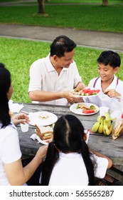 Family Sitting At Picnic Table, Father Passing Son Food