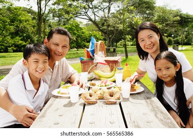 Family Sitting At Picnic Table, Looking At Camera