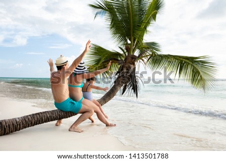 Family Sitting Together On Crooked Palm Tree Trunk Enjoying Together On Sand At Beach