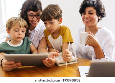 Family sitting together at table using digital tablet. Woman with kids looking at laptop with her partner drinking coffee and smiling. - Powered by Shutterstock