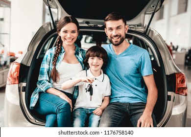 Family Are Sitting In The Trunk Of A New Car. Smiling Customers. Buying In A Showroom. Automobile Salon. Happy Together. Successful Choice. Good Mood. Great Trade. Auto Rewiew. Make A Decision.