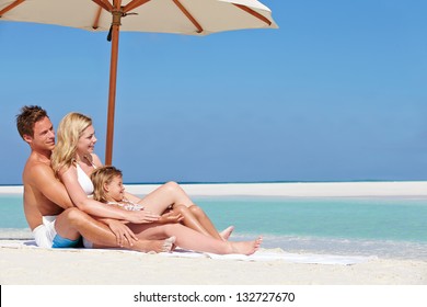 Family Sitting Under Umbrella On Beach Holiday