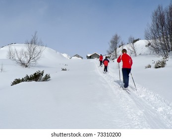 Family At Ski At A Light Up Hill Heading Towards A Hunting Lodge In The Norwegian Mountains At Easter