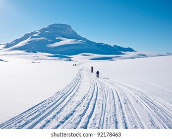 Family skiing in a groomed curved multiple ski track heading towards a characteristic mountain summits in the norwegian mountains at easter
