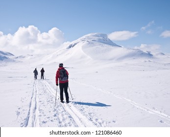 Family skiing towards a mountain pass with a characteristic mountain summit on the right in the norwegian mountains at easter