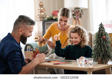 Family with small daughter indoors at home at Christmas, making Christmas cards.