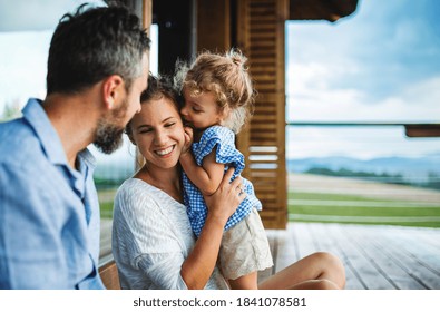 Family with small daughter sitting on patio of wooden cabin, holiday in nature concept. - Powered by Shutterstock