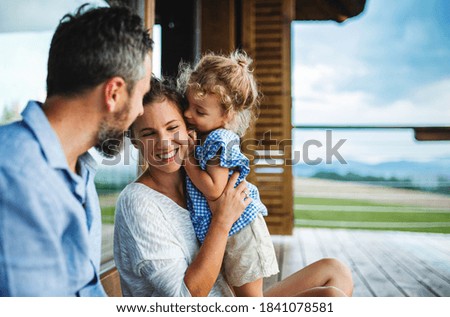 Family with small daughter sitting on patio of wooden cabin, holiday in nature concept.