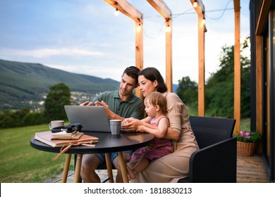 Family With Small Daughter Using Laptop Outdoors, Weekend Away In Container House In Countryside.