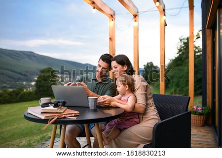 Family with small daughter using laptop outdoors, weekend away in container house in countryside.