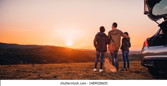Familie mit kleinem gelbem Hund, der auf Hügel geht und Sonnenuntergang sieht