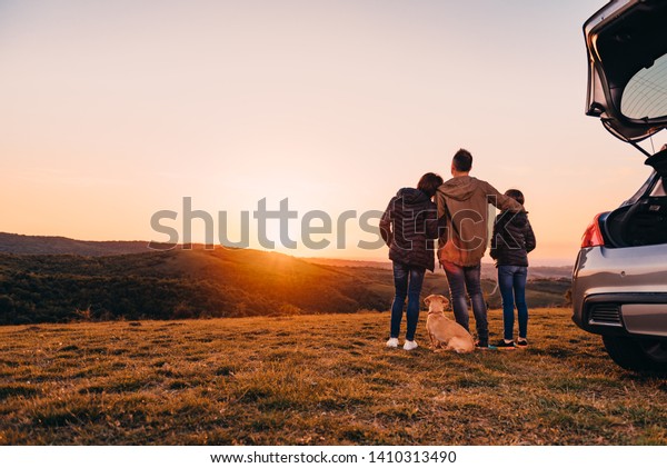 Family with small yellow dog embracing at hill and\
looking at sunset