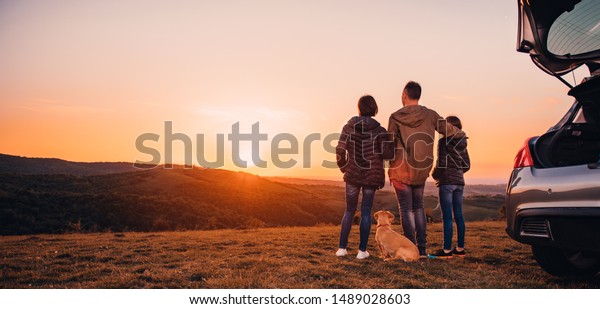 Family with small yellow dog embracing at hill and\
looking at sunset