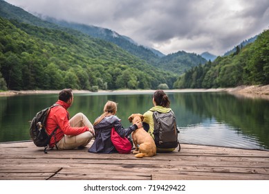 Family with a small yellow dog resting on a pier and looking at lake and foggy mountains