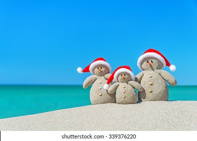 Family Of Snowmen In Santa Hats At Tropical Beach. New Year's And Christmas Holiday In Hot Countries Concept.