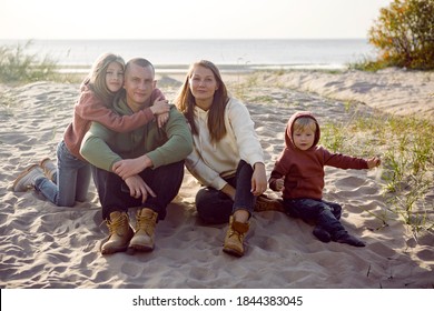 family with a son and daughter and a dog sit on the sand in autumn