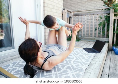 Family Sport Activity. Caucasian Mother With Toddler Son Doing Distant Remote Online Fitness Workout On House Backyard With Laptop. Parent Mom Rocking Child On Her Knees Legs. Sport At Home