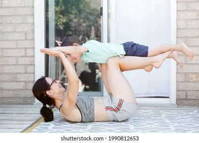 Family Sport Activity. Caucasian Mother With Toddler Son Doing Distant Remote Online Fitness Workout On House Backyard With Laptop. Parent Mom Rocking Child On Her Knees Legs. Sport At Home