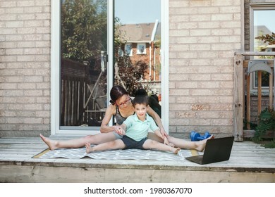 Family Sport Activity. Middle Age Caucasian Mother With Toddler Son Doing Distant Remote Online Fitness Workout On House Backyard With Laptop. Parent Exercising With Child Boy Kid. Sport At Home.